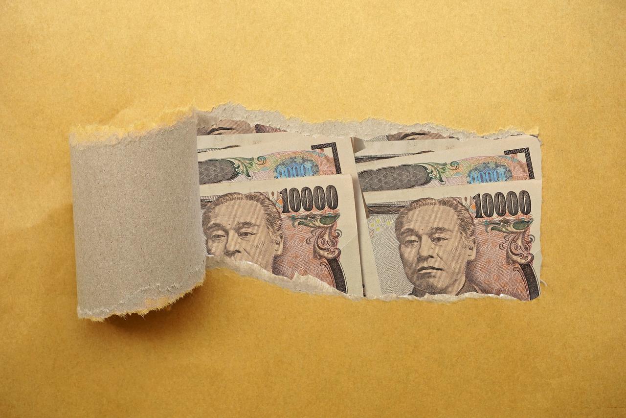 破れた紙の向こう側に覗く複数の一万円札