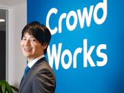 クラウドワークス社のロゴの前で微笑む吉田浩一郎社長