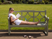 公園のベンチに寝そべって本を読む女性