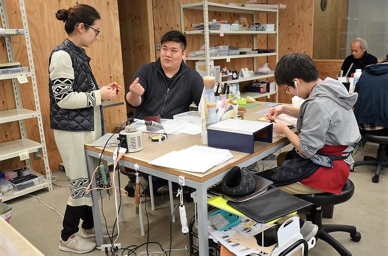 東京・東村山の自社工場で、革製品を手作る職人と話すジョッゴの高橋亮彦社長（左から2人目）。