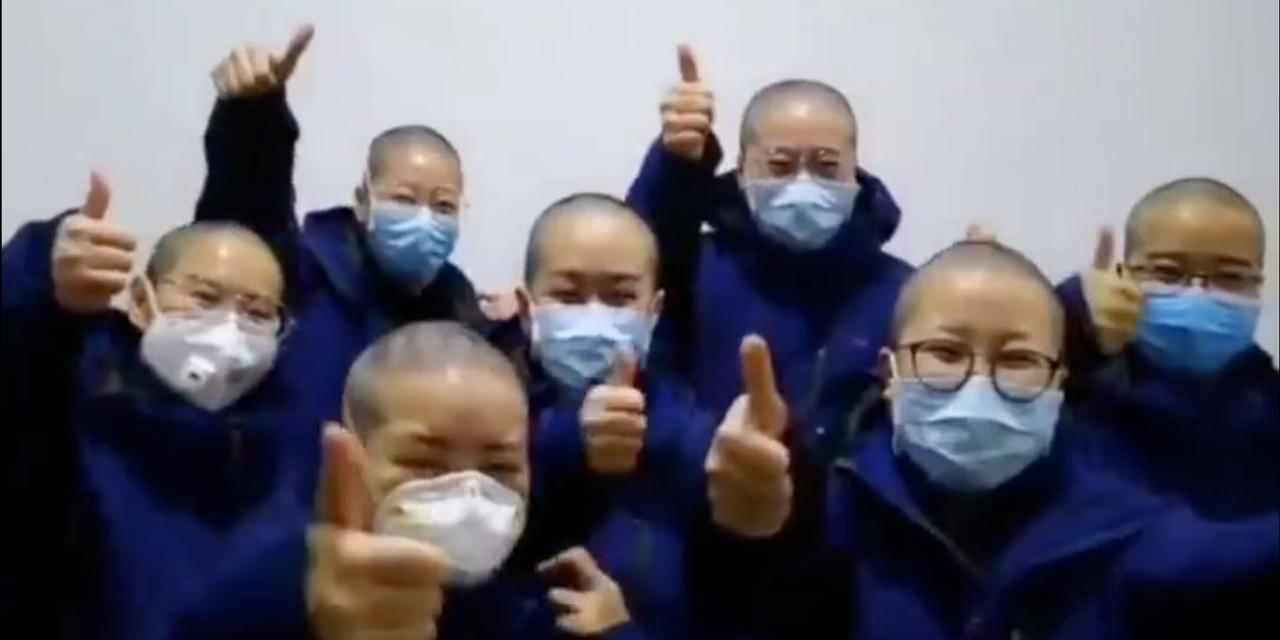 髪を剃り落とし、防護服を着てポースをとる看護師たち。中国湖北省武漢市にて。