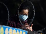 武漢の住宅街の入り口、有刺鉄線の向こう側で携帯電話を使用する女性
