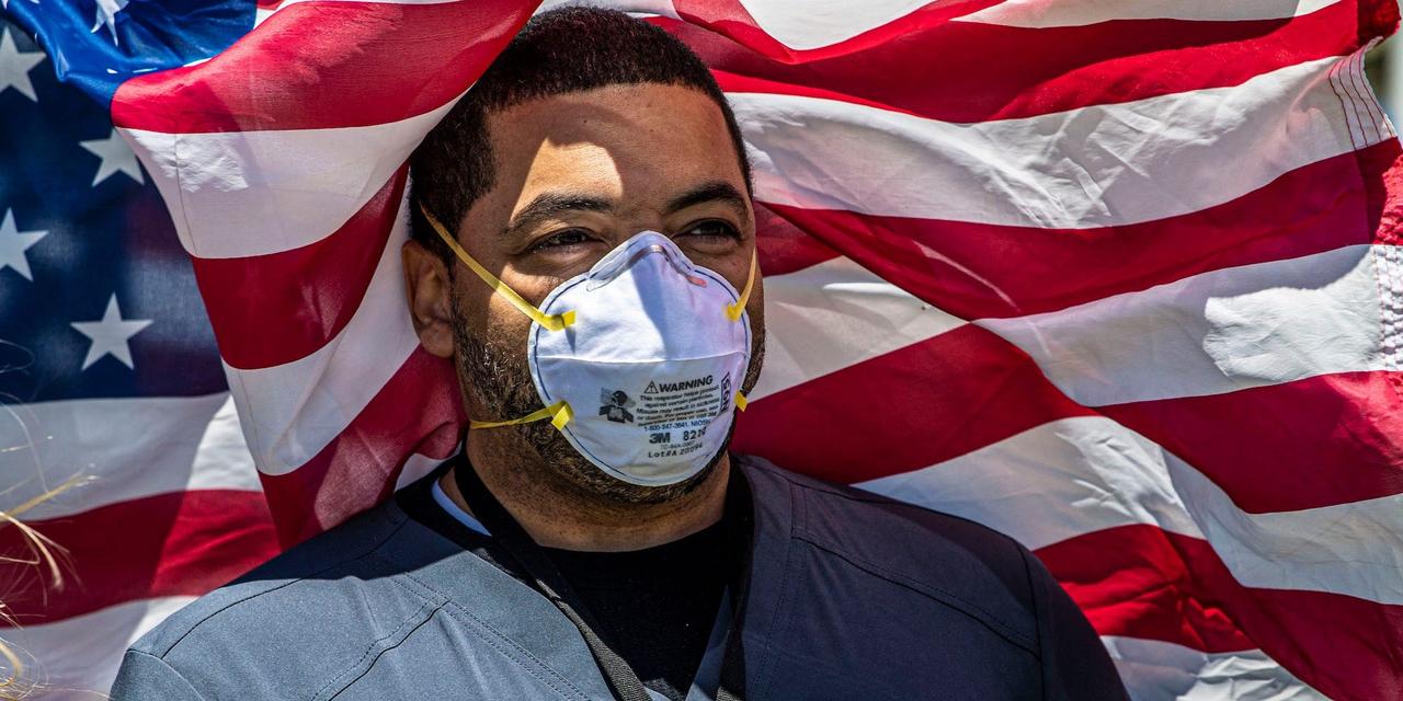 マスク姿でアメリカ国旗を背にするデレク・ワシントンさん。看護師として、ニューヨーク州イーストメドウにあるナッソー大学医療センターで勤務している。2020年5月12日。