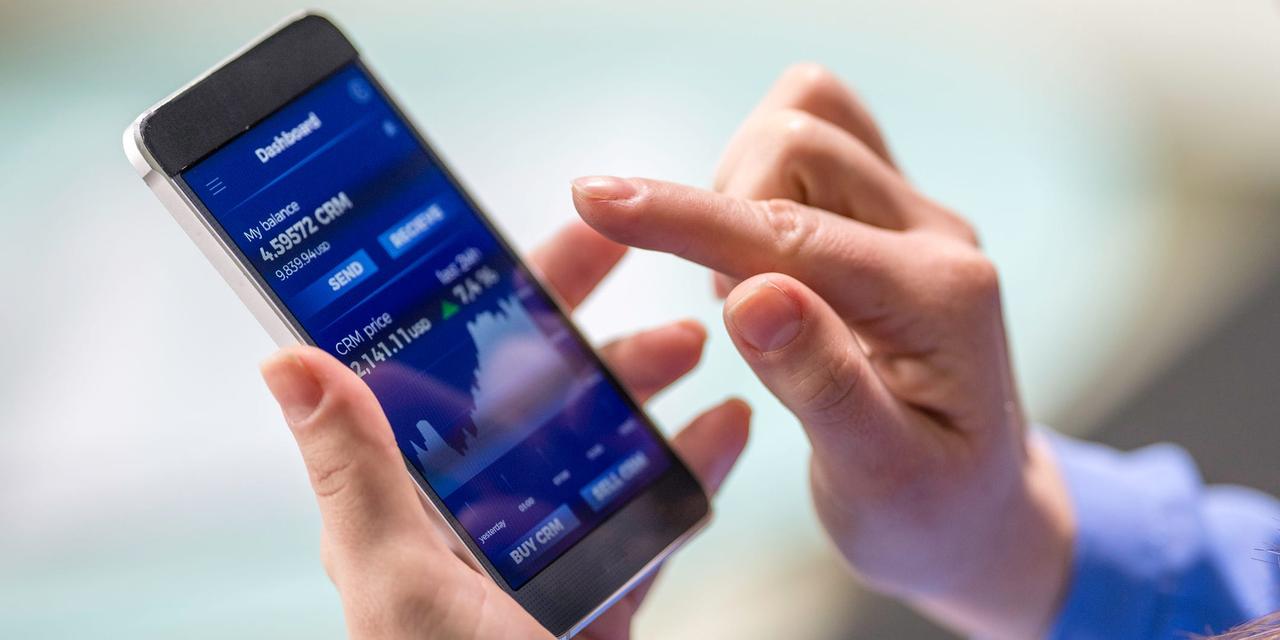 Close-up photo of a woman buying cryptocurrency through a smart phone app that is also showing the growth graph.
