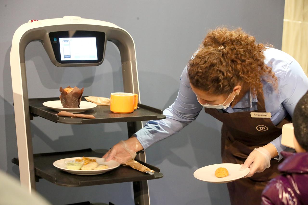 A waitress puts plates on a tray of a robot waite