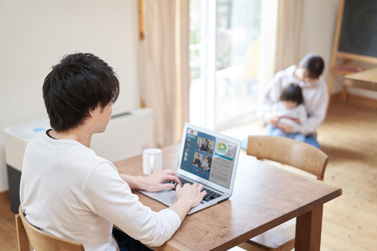 母親が子どもを見ている横でパソコンを使って仕事をする男性