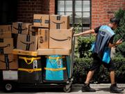 プライムデーの期間中に、大量の荷物を積んだカートを引くアマゾンの配達員。ニューヨークにて。
