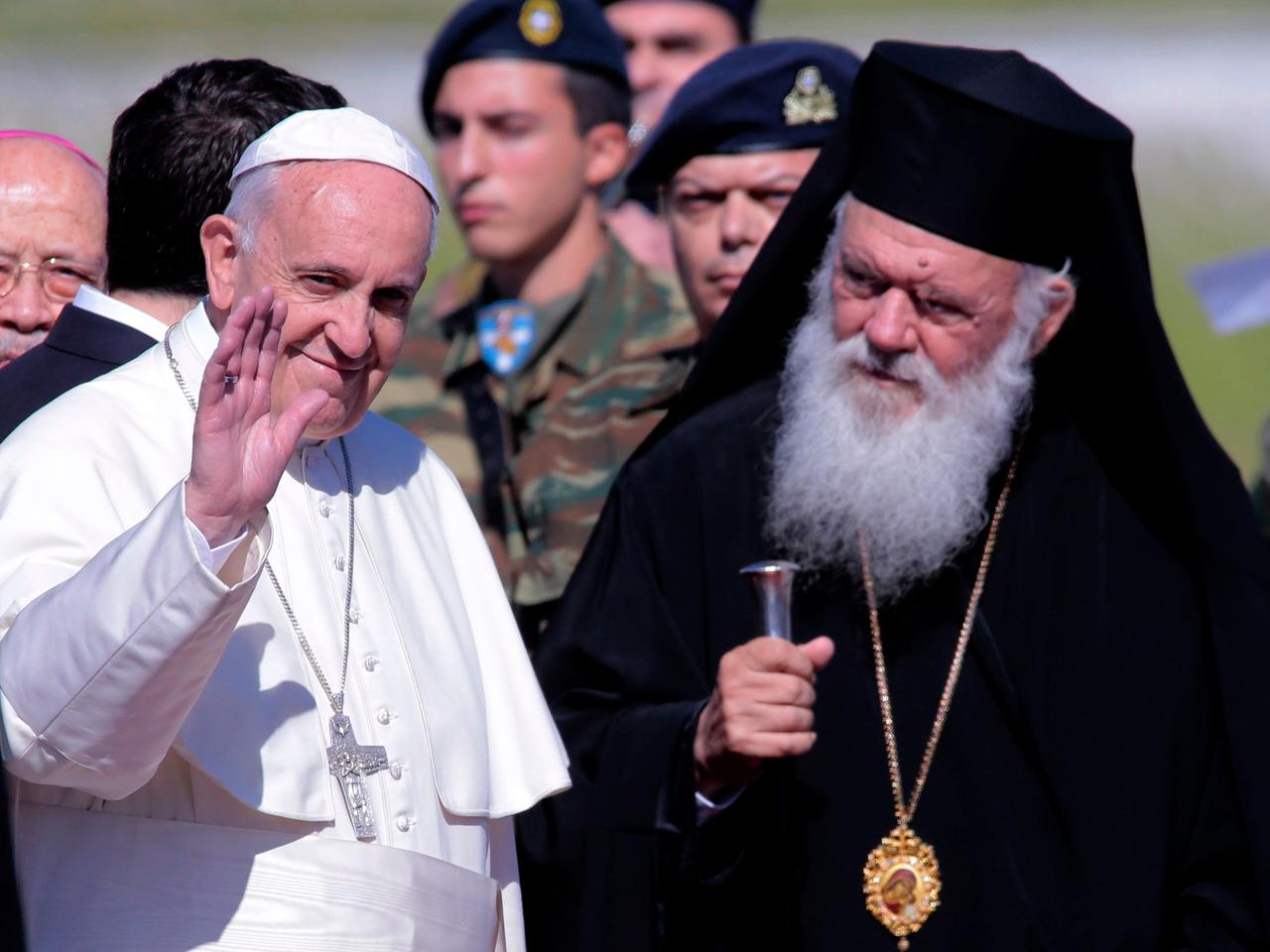 2016年4月16日、ギリシャのレスボス島のミティリーネ空港に到着し、アテネと全ギリシャの大司教イエロニモス2世（左）に出迎えられるローマ教皇フランシスコ（右）。