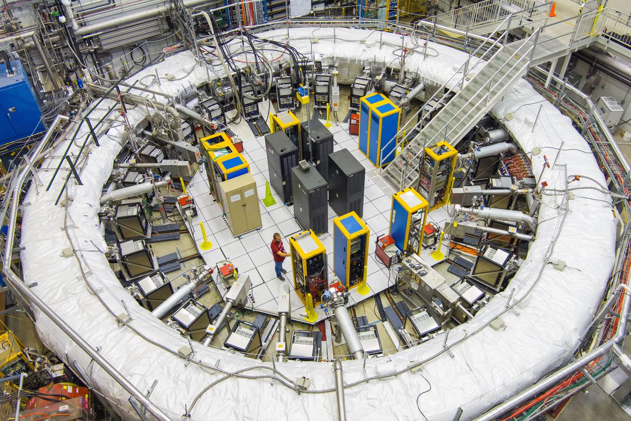 フェルミ研究所で2018年に始まった｢ミューオンg-2｣実験では、写真のリング状装置（｢g-2蓄積リング磁石｣）のなかで、光速に近いスピードでミューオンを周回させる。