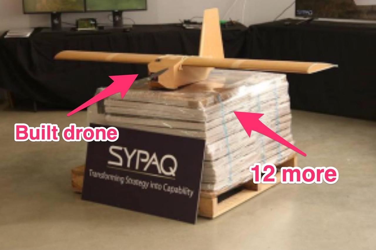 組み立てられたSYPAQのドローンが、平らに梱包された状態のドローンの積み重ねの上に置かれている。