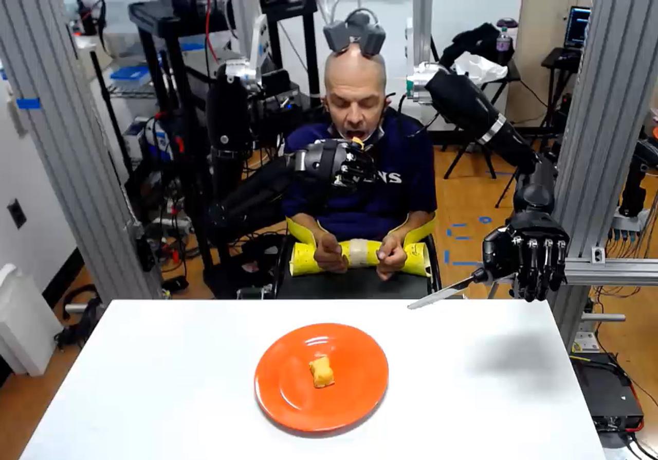 SF世界が現実に。脳の電極でロボット・アームを操作しスポンジ菓子を食べる男性