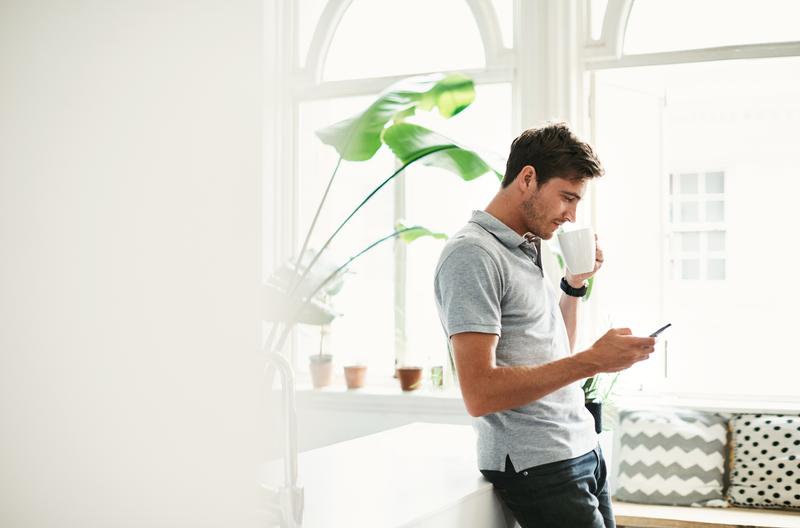 自宅でコーヒーを飲みながらスマホを操作する男性