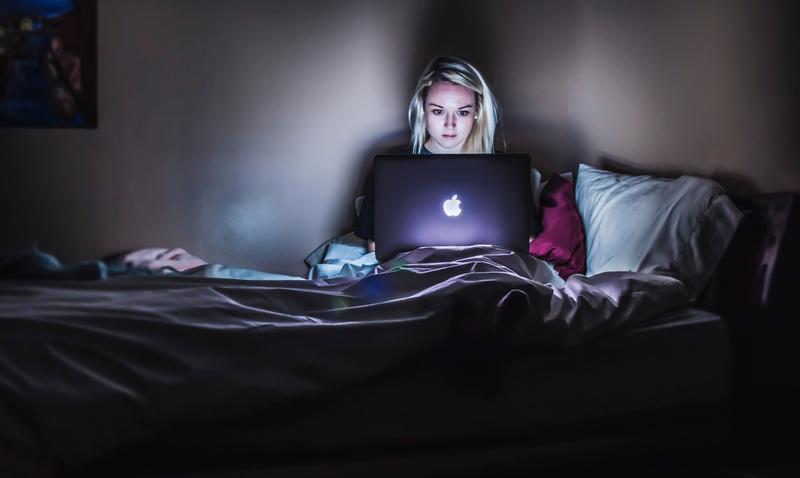ベッドの上でノートパソコンを開く女性