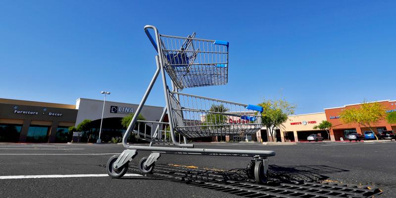 A lone shopping cart sits in an empty parking lot Friday, April 24, 2020, outside closed businesses in Phoenix. The outbreak of the coronavirus has dealt a shock to the global economy with unprecedented speed and retail stores may have been changed forever by the outbreak. (AP Photo/Matt York)