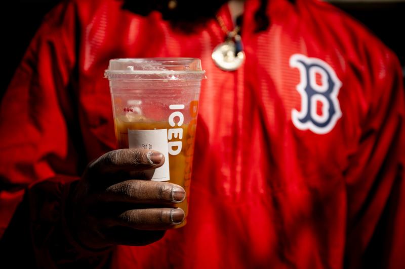 A Boston Red Sox Fan holds an iced Dunkin' coffee in their right hand.