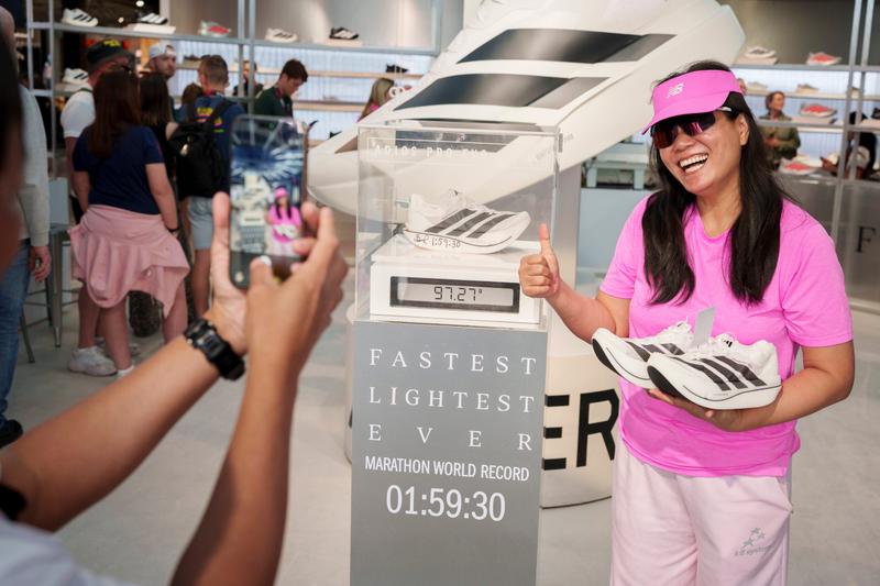 A shopper at the Adidas running hub in London holds up the Adizero Adios Pro Evo 3 shoes while standing by the signed Sabastian Sawe shoe.