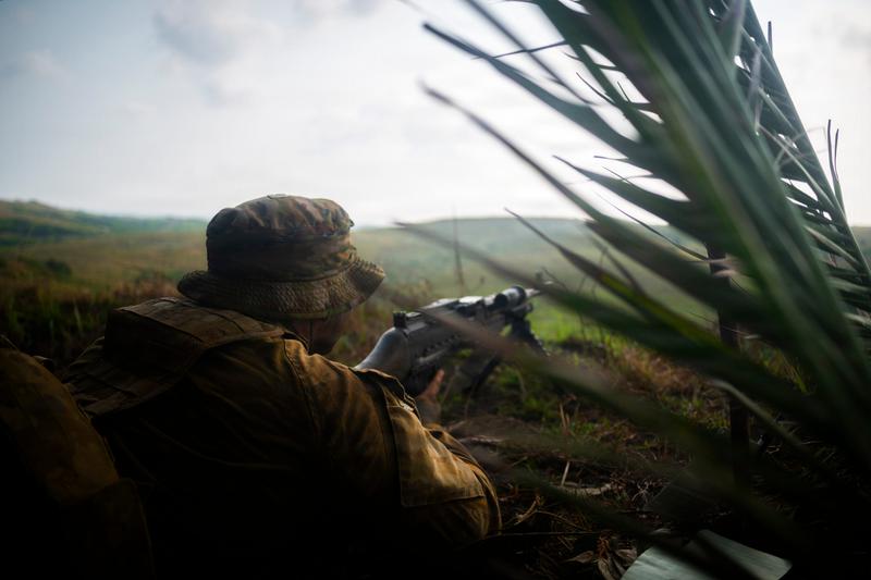 A soldier lies down holding a rifle pointing it out towards a field.
