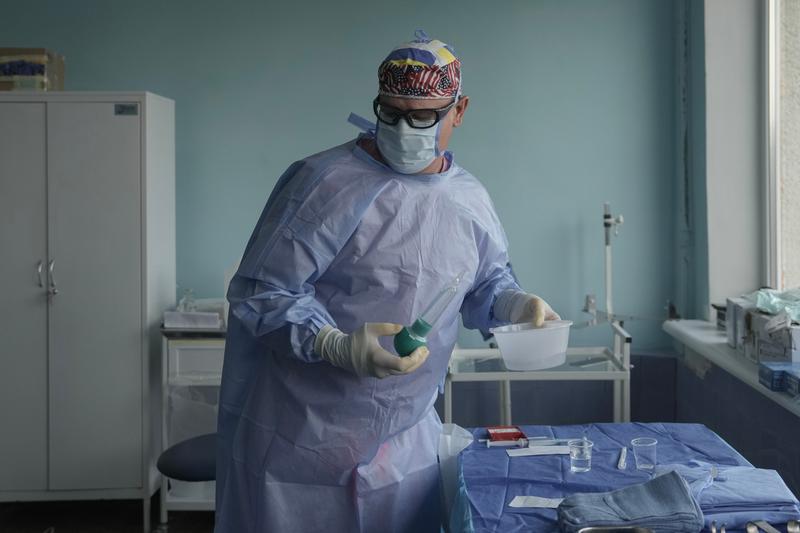 A nurse wears blue protective clothing and an American flag headband while carrying a plastic container and a syringe.
