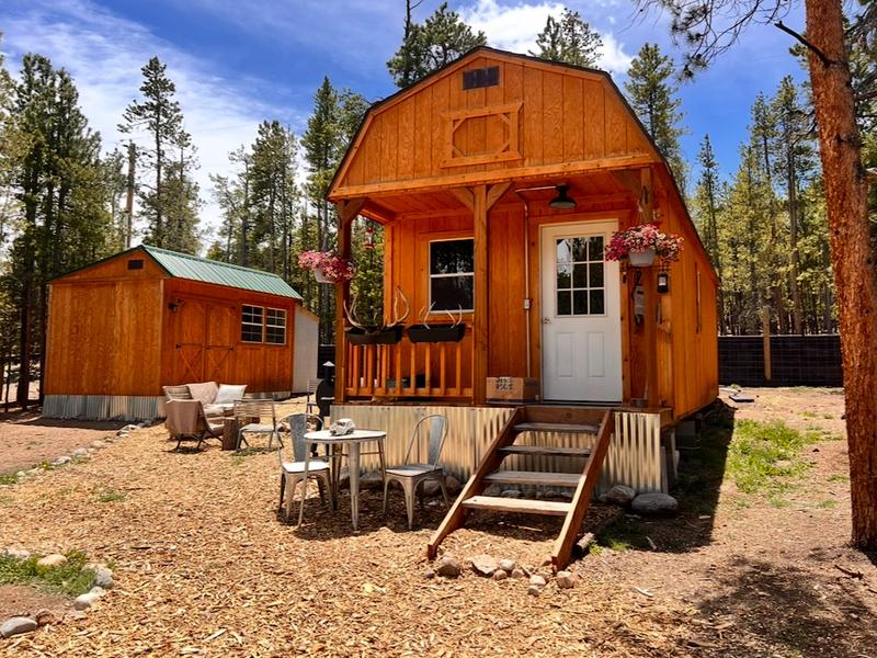 A wood tiny house with seating in front of it.