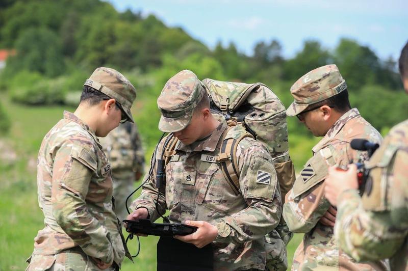 A group of soldiers stands around a tablet in the forest.