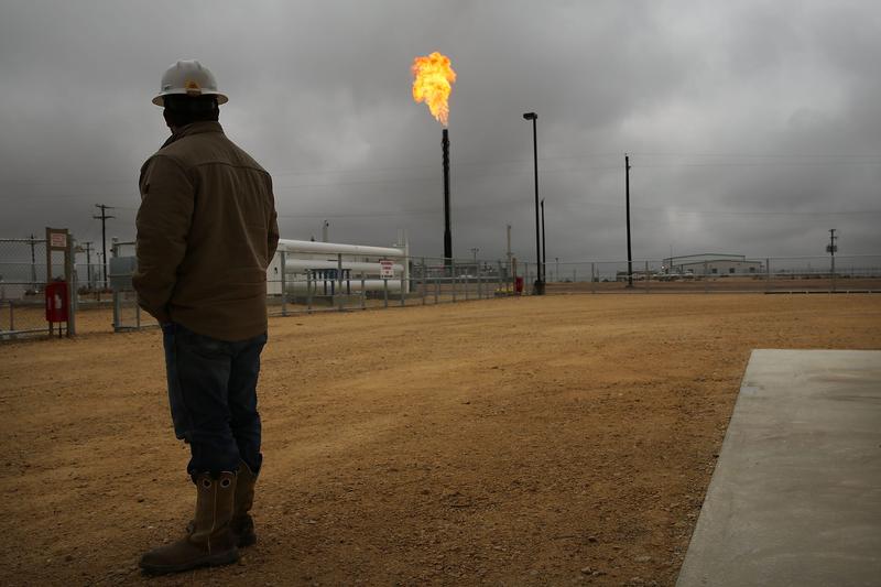 A man stands in front of a natural gas plant that's flaring in Texas