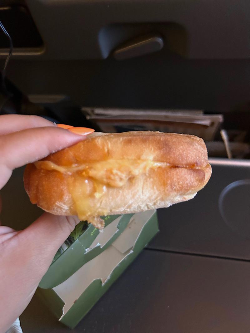 A hand holding a sandwich filled with melted cheese.