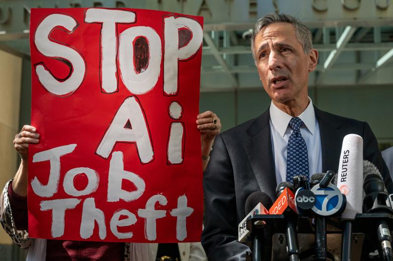 Attorney William Savitt, representing OpenAI, speaks during a news conference outside federal court in Oakland, California, with a sign reading "Stop AI job theft" next to him.