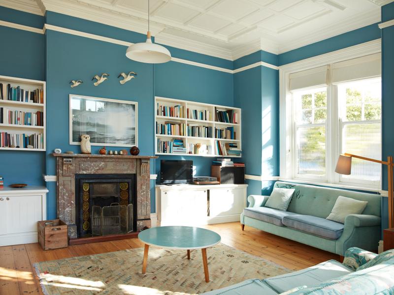 A living room with blue walls, open bookshelves, and lots of decor.