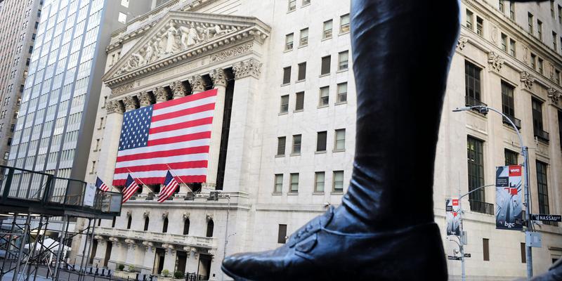 Boot of a statue photographed in front of the New York Stock Exchange and the American flag