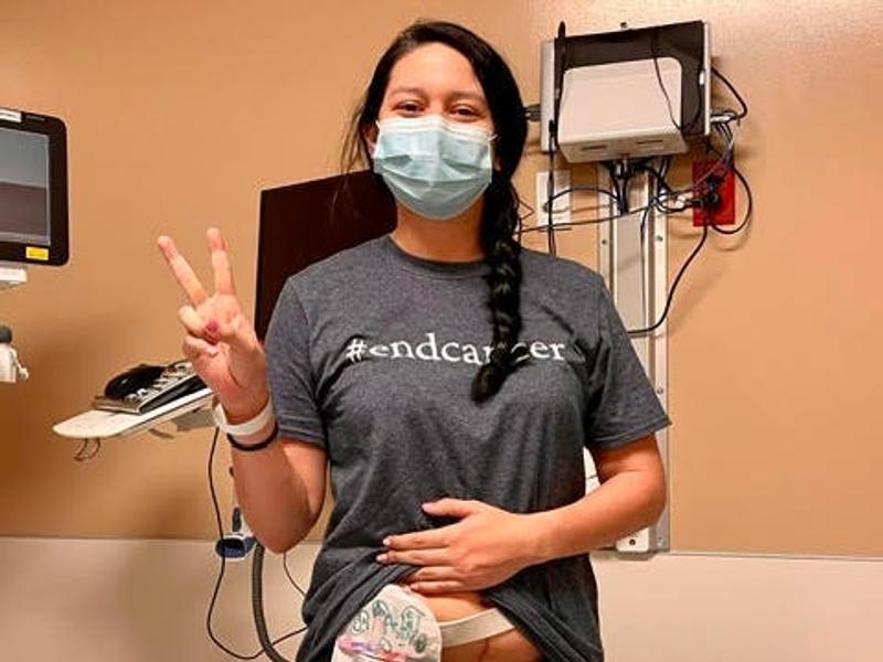 A woman in a mask and shirt that reads "end cancer" in a hospital with medical equipment