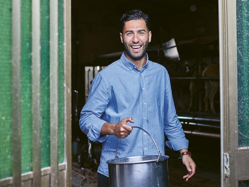 A man walking out of a diary holds a bucket.