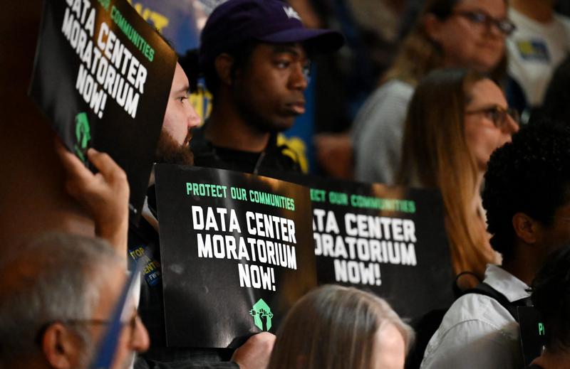Protesters hold signs calling for a data center moratorium