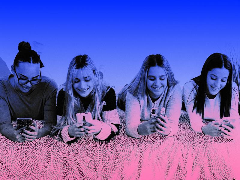 Four teenage girls sitting together and scrolling on their cell phones.