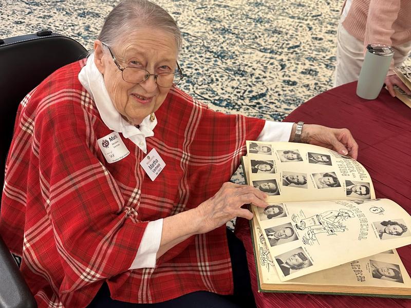 An older woman in a wheelchair looking at a high school yearbook.