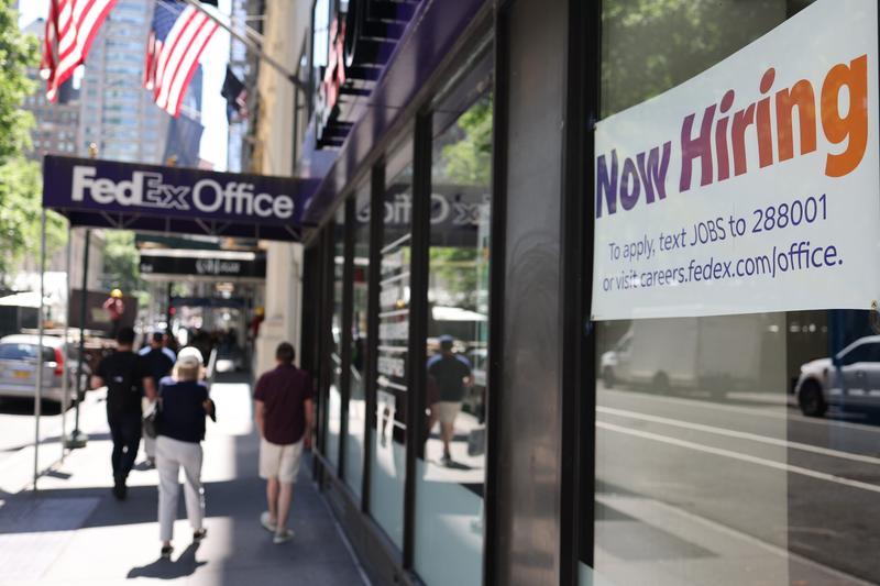 A "Now Hiring" sign is seen at a FedEx location window