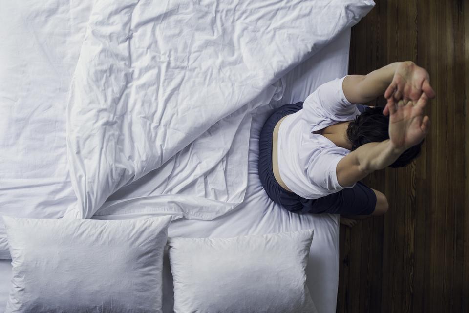 ベッドの上で伸びをする男性