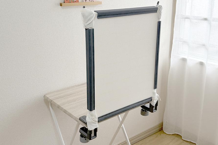 Small tabletop tufting frame clamped to a desk with white primary tufting cloth stretched tight.