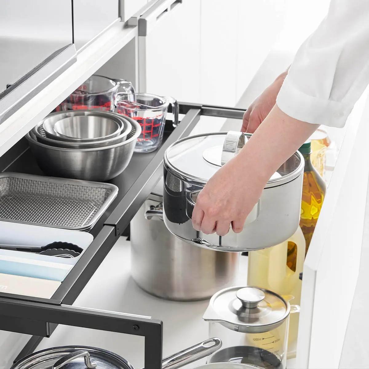 山崎実業 「シンク下引き出し幅伸縮スライドラック タワー D30」の天板をスライドさせ下段にものを収納する様子