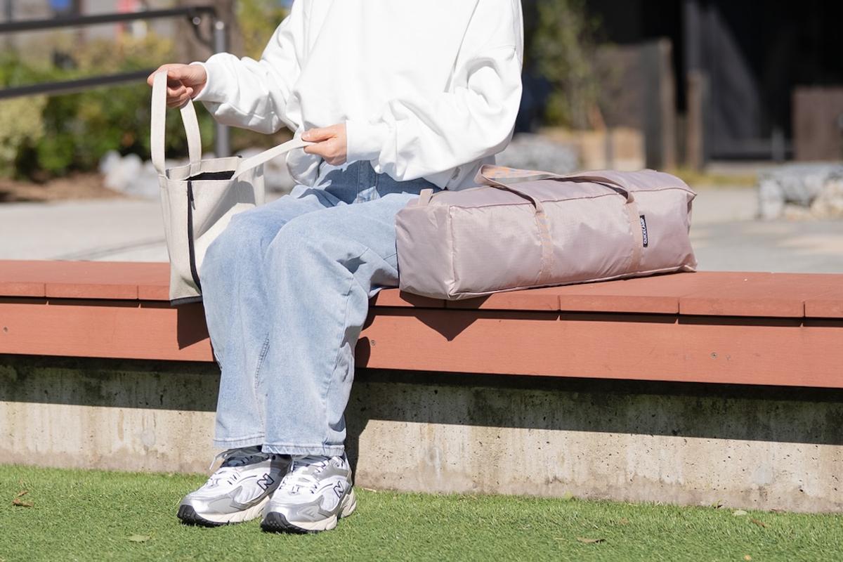 クイックキャンプのコンパクトシェードをベンチに置いてその隣に座る女性