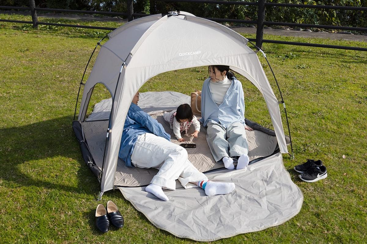 芝の上に置いたクイックキャンプのコンパクトシェードの中でくつろぐ家族