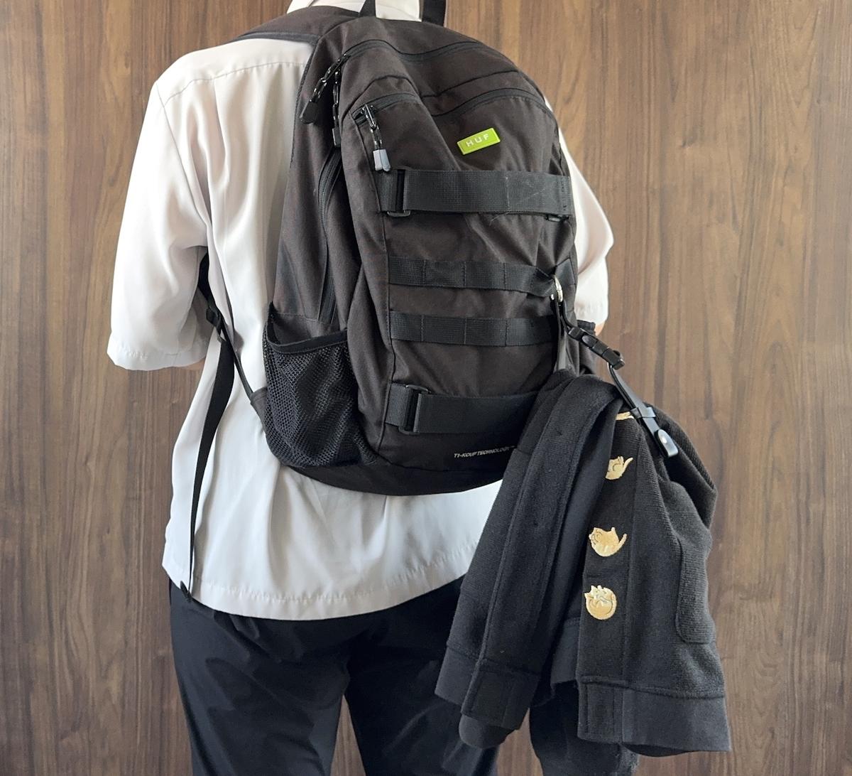 背負った黒いリュックに付いた3COINSのジャケットホルダーに黒い上着を引っ掛けている人の後ろ姿