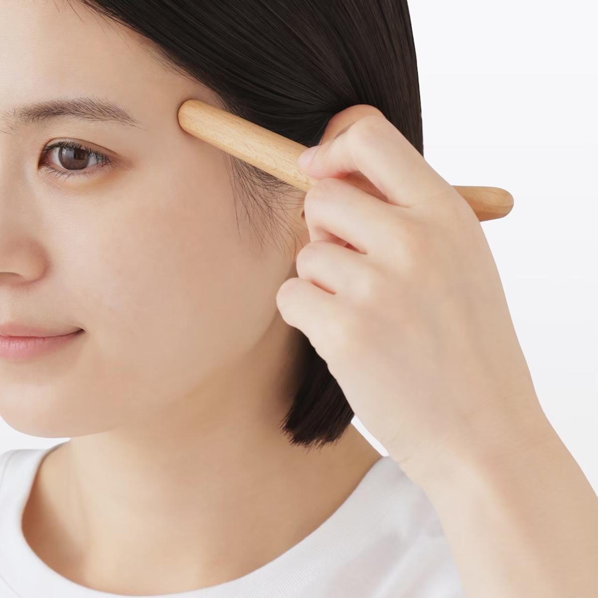 無印良品「ブナ材マッサージスティック」の先端をこめかみにあてている様子